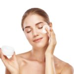 Anti-Ageing Products. Portrait of healthy young woman with closed eyes applying moisturizer cream on