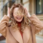 smiling woman walk in center and protect hair from wind gust at street. girl hands straighten hair